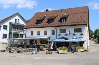 In Zeihen (5079, Kanton Aargau) steht das Restaurant Roessli-Stuebli mit weisser Fassade, roten Blumenkasten und Sonnenschirmen an der Strassenecke.