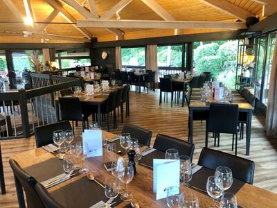 Im Restaurant Tee Off in Bougy-Villars (1172, Kanton Waadt) sind die Tische elegant mit Glasglaesern und Menukarten gedeckt, in einem modernen Raum mit Holzdecke und grossen Fenstern.