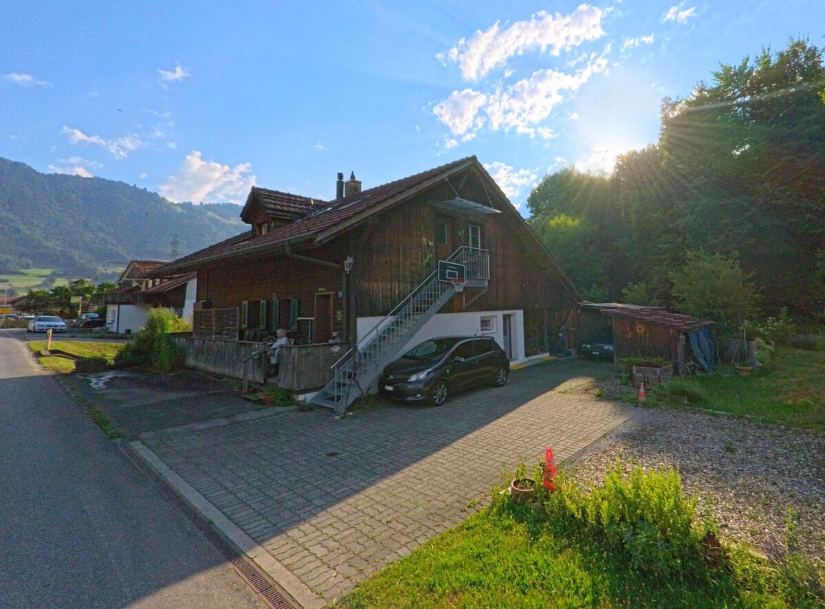 Am Waldrand von Reutigen (3647, Kanton Bern) steht ein Wohnhaus mit Aussentreppe und Basketballkorb, umgeben von Gartenfläche und angrenzender Naturkulisse im Gegenlicht der Sonne.
