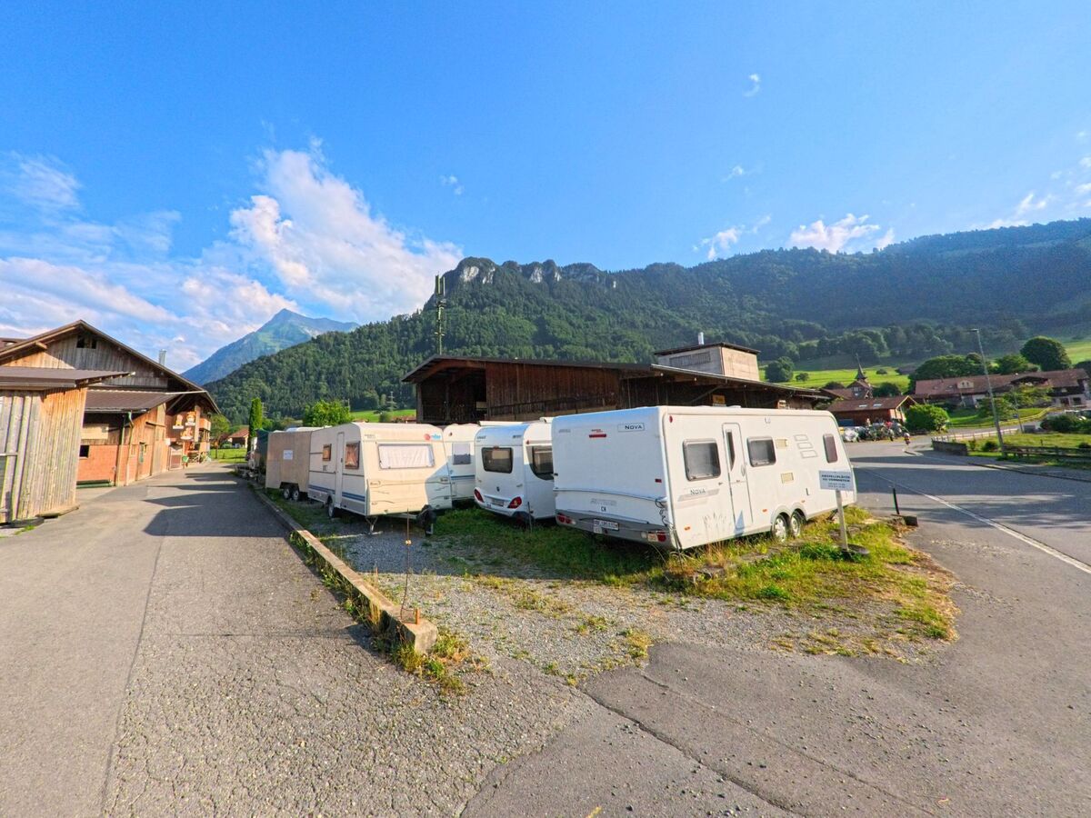 In Reutigen (3647, Kanton Bern) stehen mehrere Wohnwagen auf einem Abstellplatz neben landwirtschaftlichen Gebäuden, mit Blick auf bewaldete Hügel und eine markante Felsformation.
