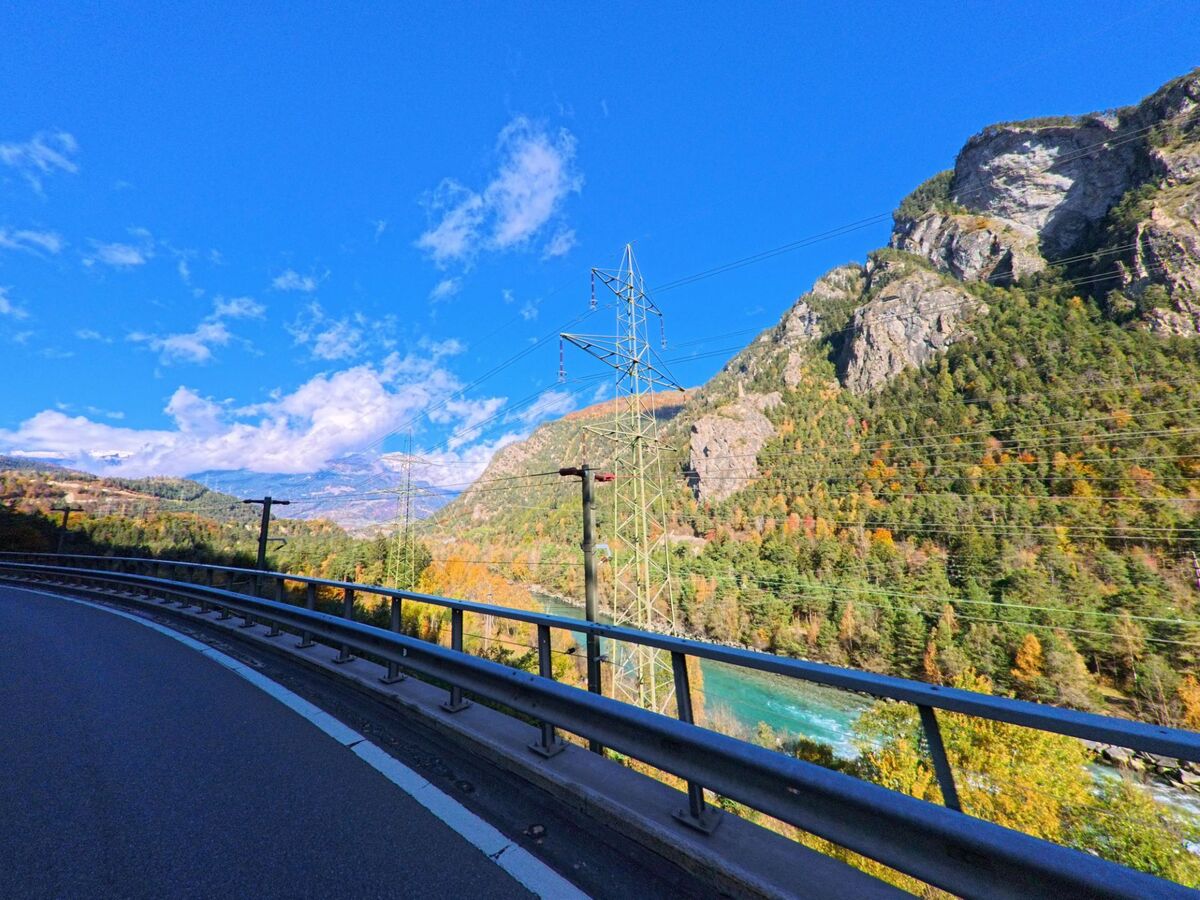 Entlang einer kurvigen Strasse bei Rhäzüns (7403, Kanton Graubünden) führt der Blick über eine Brücke auf den Fluss im Tal, eingerahmt von steilen Felswänden und herbstlich gefärbten Wäldern.
