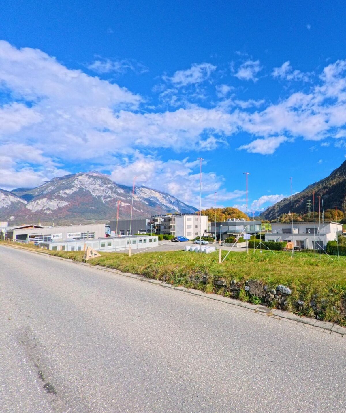 Am Rand eines Gewerbegebiets in Rhäzüns (7403, Kanton Graubünden) liegen moderne Betriebsgebäude vor offenen Grünflächen und einem weiten Blick auf die umliegenden Bergzüge.