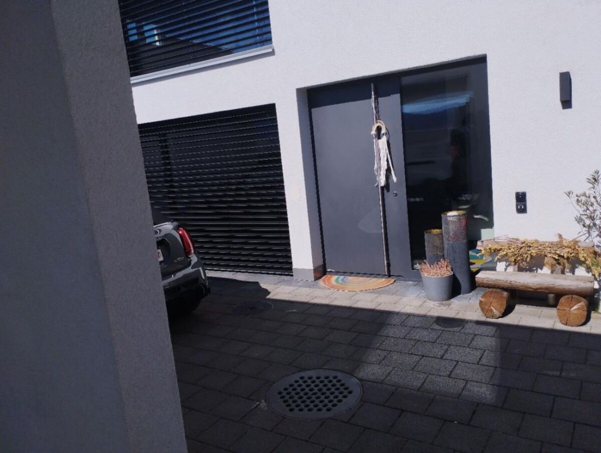 Vor einem modernen Eingangsbereich in Rheinau (8462, Kanton Zürich) stehen Pflanzkübel, dekorative Holzstämme und eine Sitzbank aus Baumstämmen neben einer dunklen Tür mit Wanddeko.