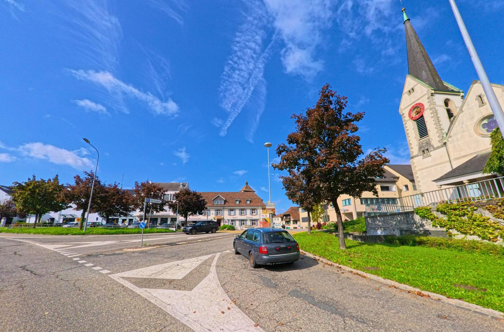 In Rheinfelden (4310, Kanton Aargau) zeigt sich das Stadtzentrum mit einer Kirche und angrenzenden Wohnhaeusern unter blauem Himmel.