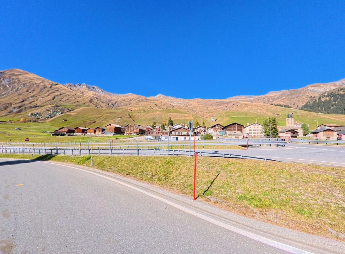 Vor den sanften Berghängen erstreckt sich in Rheinwald (7437, Kanton Graubünden) ein Dorfkern mit Holzhäusern und Kirche, erschlossen durch eine Strasse am offenen Talboden.