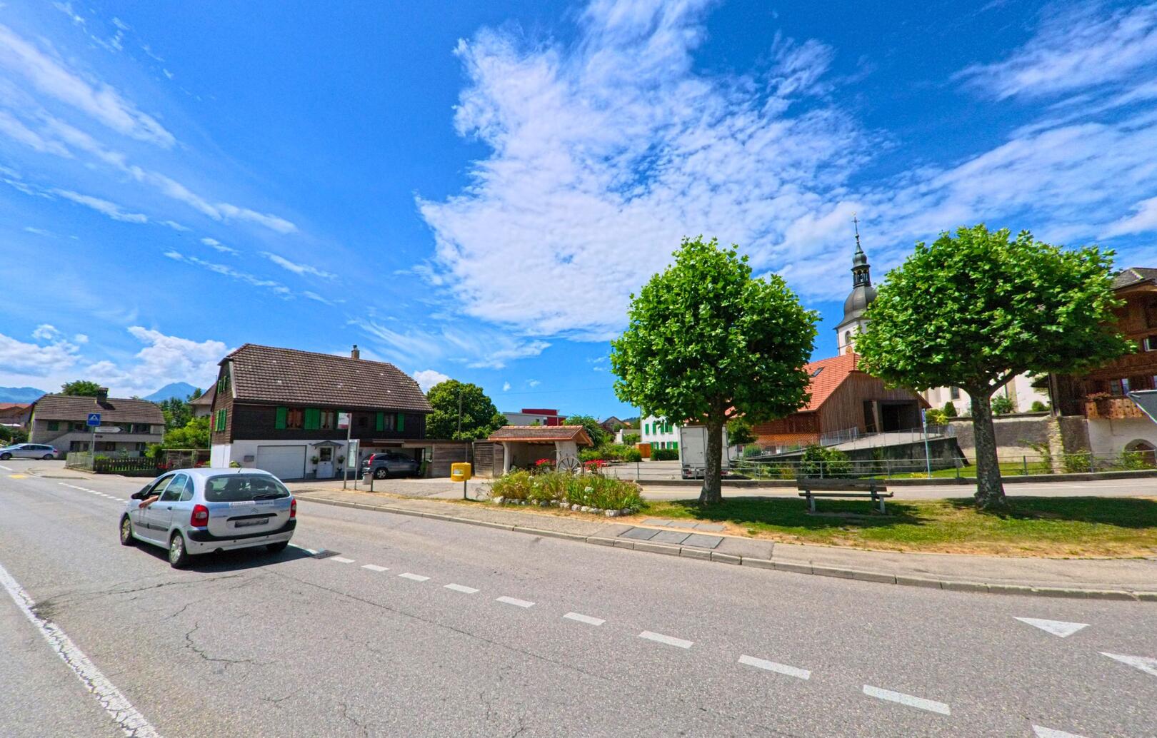 Im Zentrum von Riaz (1632, Kanton Freiburg) verläuft eine breite Strasse an gepflegten Häusern und einer markanten Kirche mit Zwiebelturm vorbei.