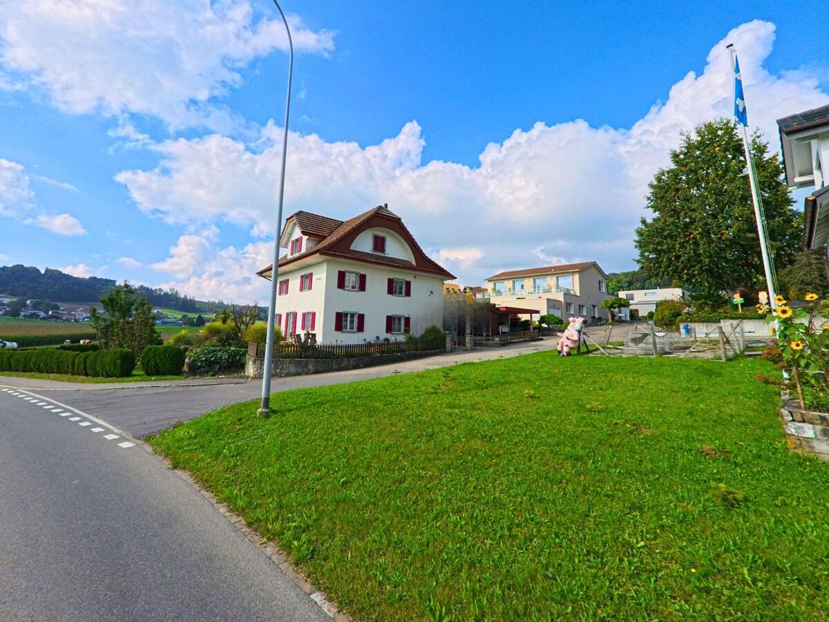 An einer leicht ansteigenden Strasse steht ein Wohnhaus mit Grünfläche in Rickenbach (6221, Kanton Luzern).