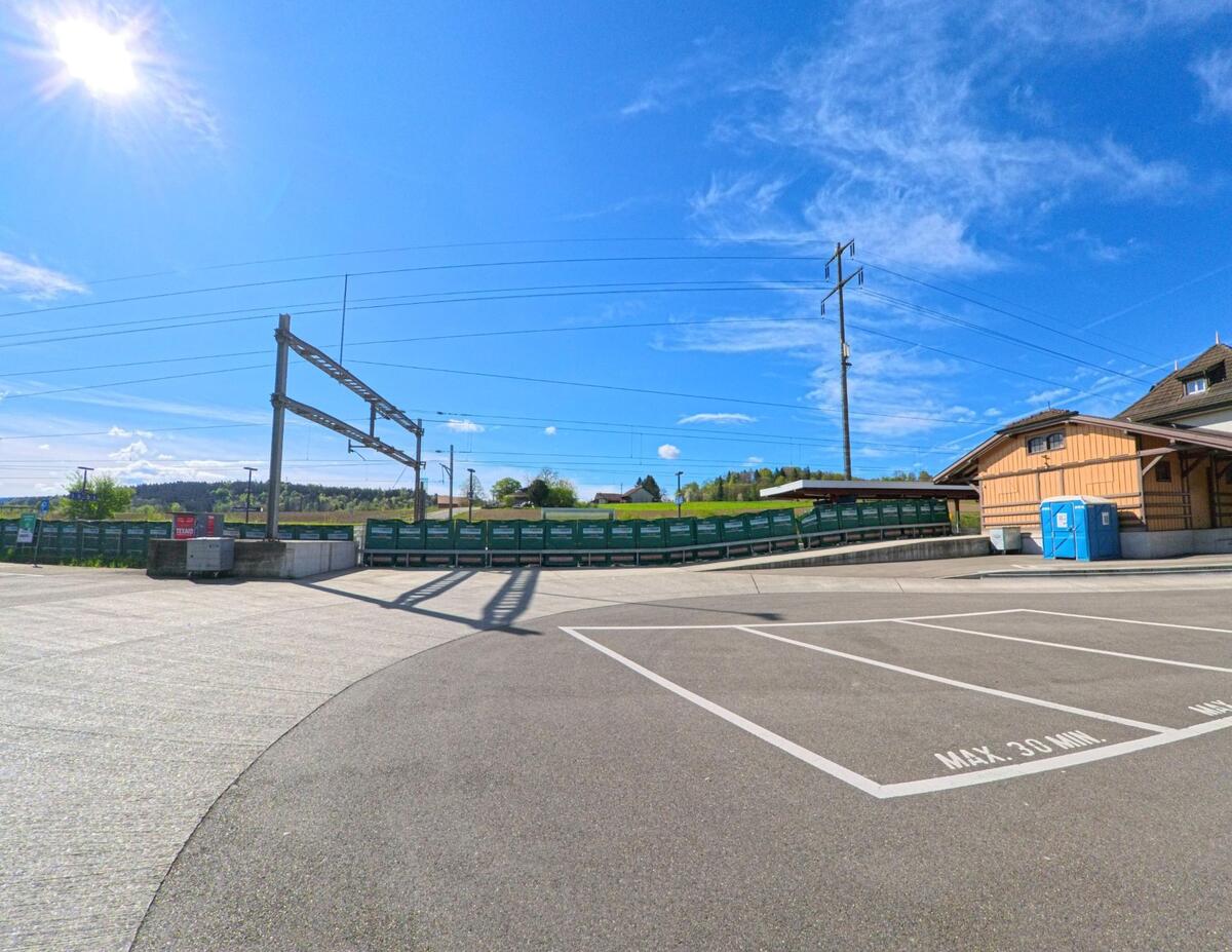 Neben dem Bahnhofsgelände in Rickenbach (8544, Kanton Zürich) befindet sich ein leerer Parkplatz mit Sicht auf Bahngleise und Gütercontainer.