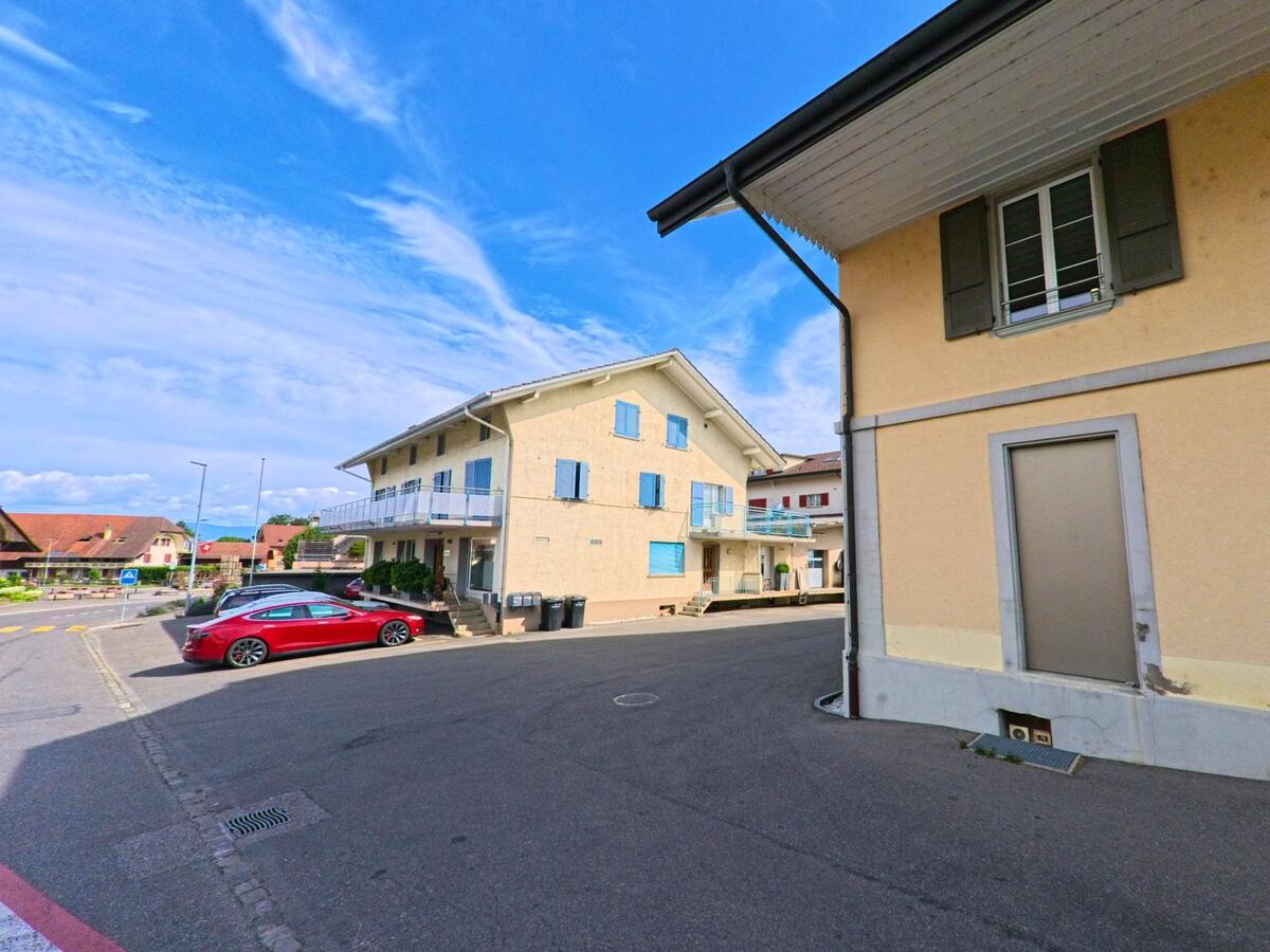 In Ried bei Kerzers (3216, Kanton Freiburg) säumen moderne Mehrfamilienhäuser mit farbigen Fensterläden eine ruhige Seitenstrasse im Ortskern.