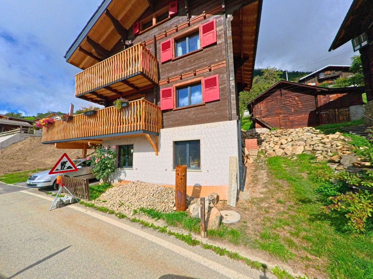 Ein traditionelles Wohnhaus mit roten Fensterlaeden und Holzbalkonen steht in Riederalp (3986, Kanton Wallis) direkt an einer kleinen Strasse.