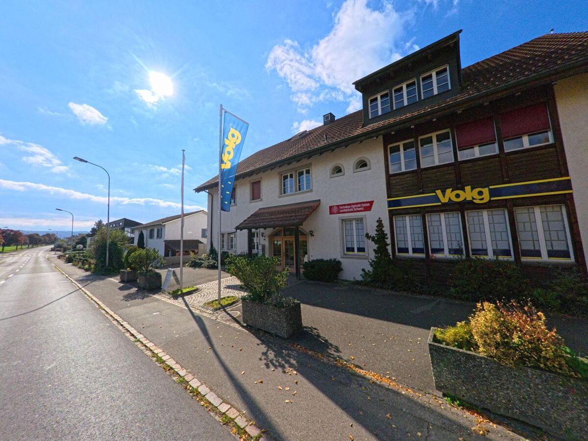 An der Hauptstrasse in Riniken (5223, Kanton Aargau) befindet sich ein Volg-Laden mit angrenzender Gemeindeverwaltung unter blauem Himmel.