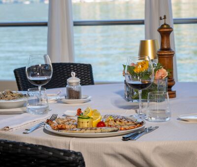 Im Ristorante Chalet San Giorgio in Brusino Arsizio (6827, Kanton Tessin) steht ein liebevoll gedeckter Tisch mit Wein und Meeresfruechten direkt am Seeufer.