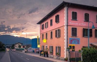 In Cugnasco (6516, Kanton Tessin) steht das Ristorante Pizzeria Del Ponte in einem rosa Gebaeude an der Hauptstrasse, waehrend im Hintergrund die Sonne hinter den Bergen untergeht.