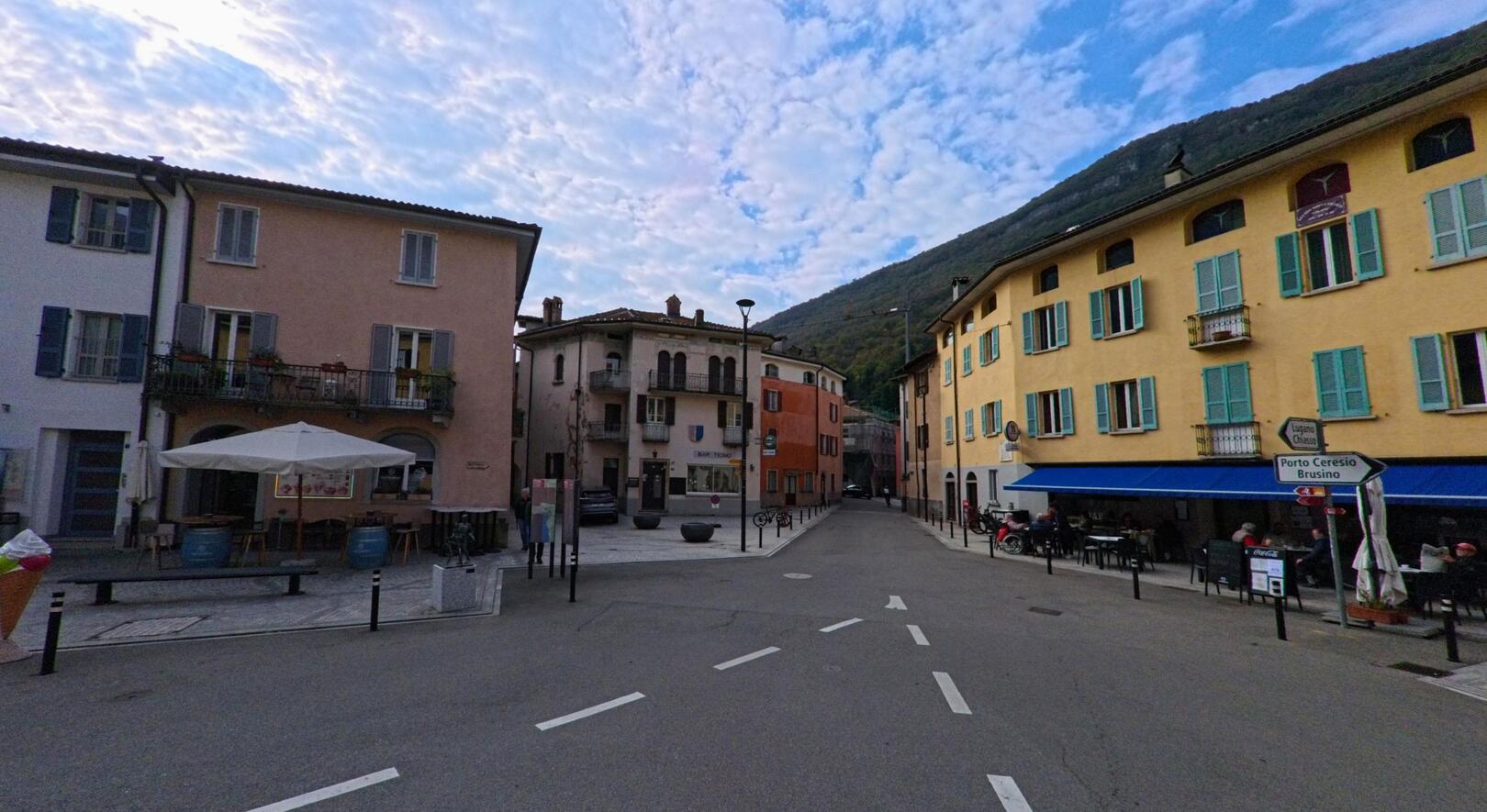 In der Altstadt von Riva San Vitale (6826, Kanton Tessin) treffen farbenfrohe Fassaden und enge Gassen aufeinander, im Hintergrund erhebt sich der bewaldete Hang.