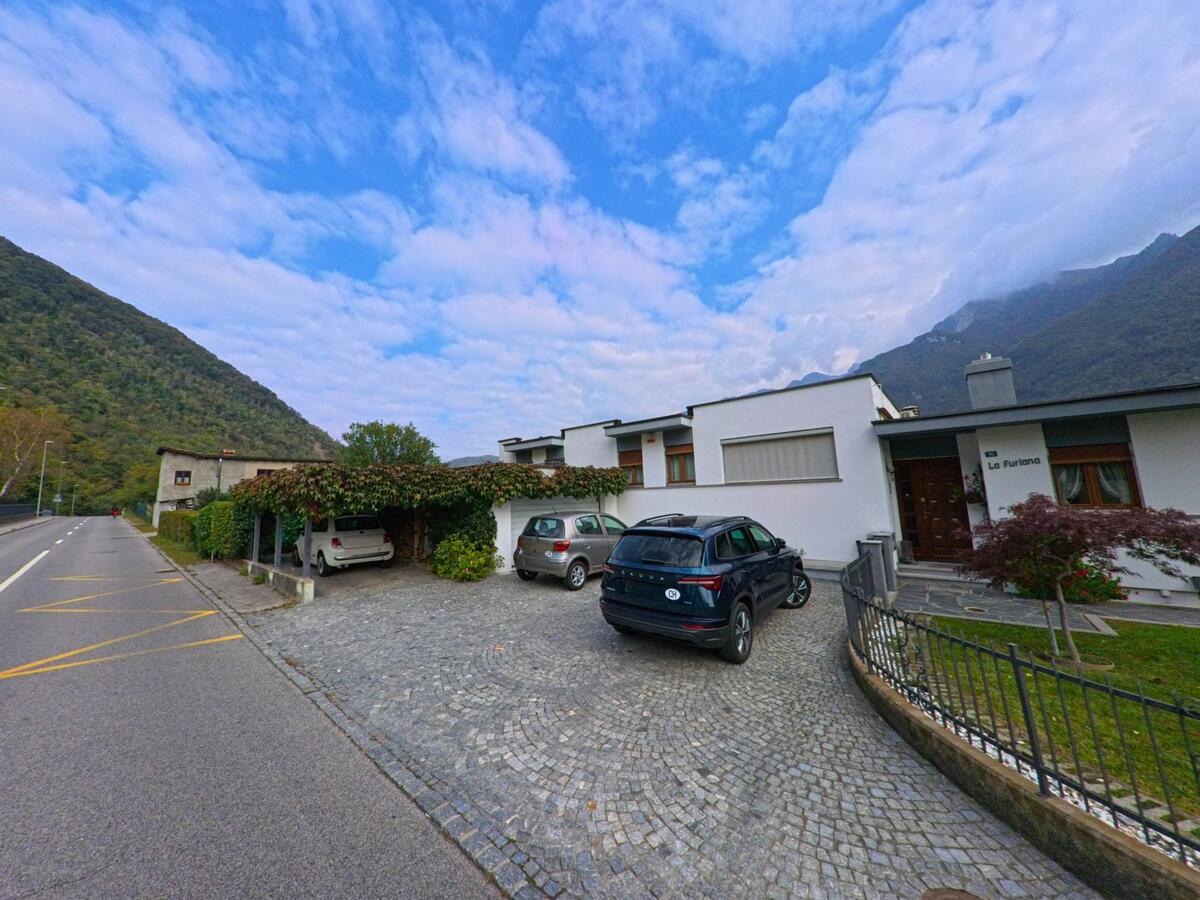 Am Rand von Riva San Vitale (6826, Kanton Tessin) stehen moderne Einfamilienhaeuser mit Einfahrten und Blick auf die bewaldeten Huegel.