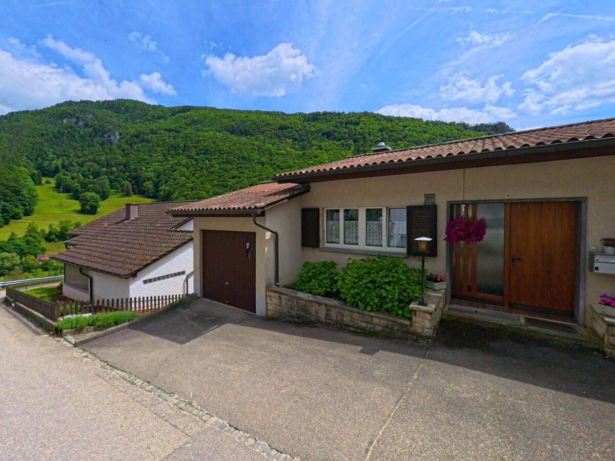 Dieses Einfamilienhaus in Roches (2762, Kanton Bern) liegt an einem Hang mit Blick auf grüne Wälder und Wiesen und besitzt eine integrierte Garage und einen gepflegten Eingangsbereich.