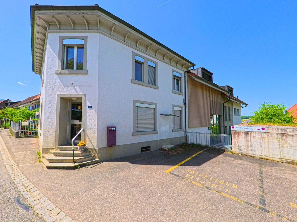 In Rodersdorf (4118, Kanton Solothurn) befindet sich ein Eckgebäude mit Eingangstreppe und Raiffeisen-Beschriftung auf dem Parkplatz neben einer ruhigen Seitenstraße.