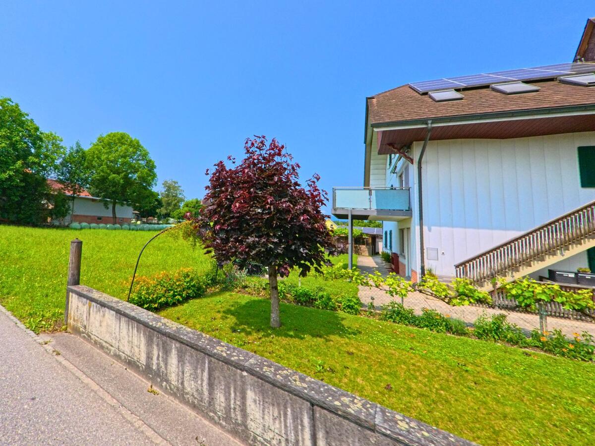 In Röthenbach (3373, Kanton Bern) steht ein Wohnhaus mit Solaranlage und Aussentreppe an einer ruhigen Strasse, umgeben von Rasenflächen und Ziersträuchern.