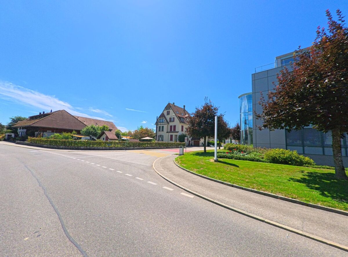 In Roggwil (4914, Kanton Bern) treffen moderne Architektur mit Glasfassade und traditionelle Wohnbauten aufeinander, eingerahmt von Baeumen und gepflegten Gruenanlagen.