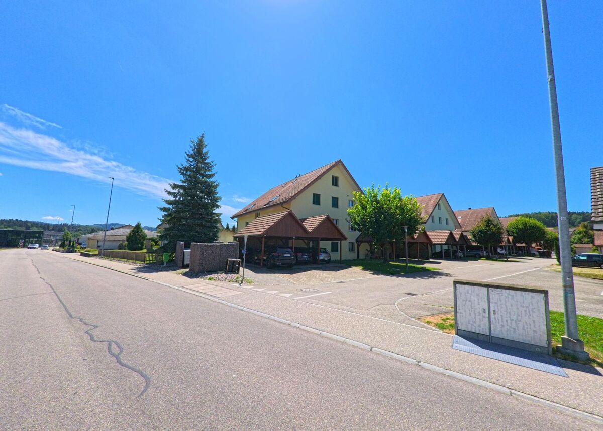 In einem ruhigen Wohngebiet von Roggwil (4914, Kanton Bern) stehen Reihenhaeuser mit Carports und kleinen Vorgartenanlagen entlang einer breiten Strasse.