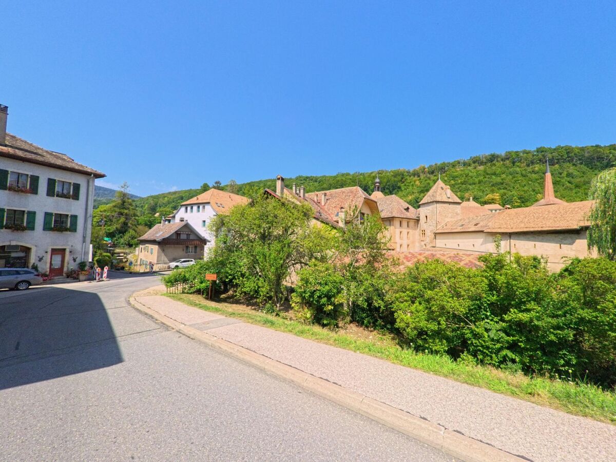 In Romainmotier-Envy (1323, Kanton Waadt) praegen die Abtei und angrenzende Haeuser mit roten Daechern das Dorfbild am Waldrand.