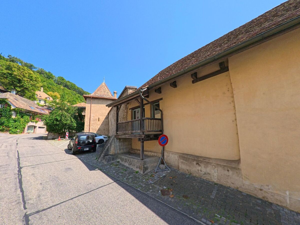 In Romainmotier-Envy (1323, Kanton Waadt) verläuft eine enge Gasse an historischen Gebäuden vorbei, darunter ein Haus mit kleinem Holzbalkon und ein runder Turm.