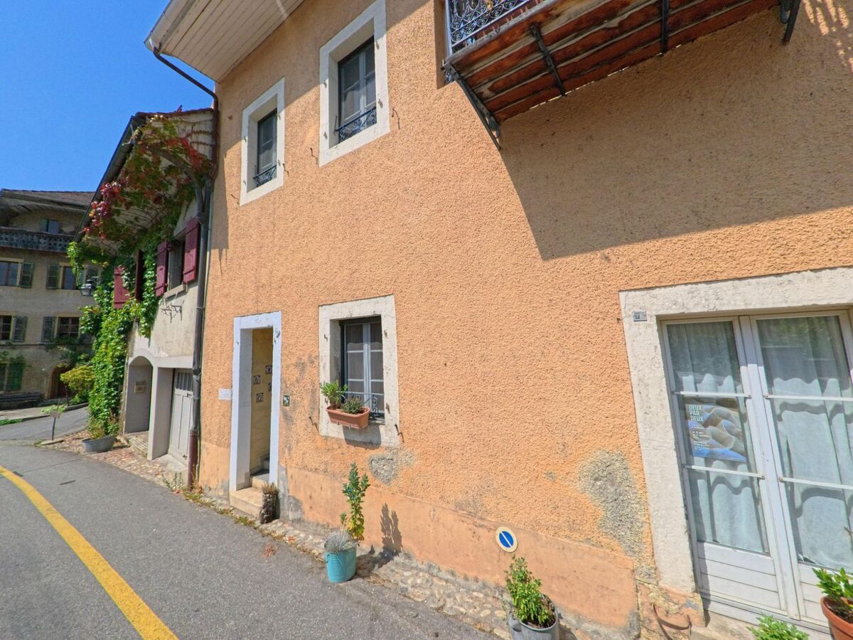 In Romainmotier-Envy (1323, Kanton Waadt) stehen an einer schmalen Strasse traditionelle Wohnhaeuser mit bunten Fensterlaeden und kleinen Balkonen.