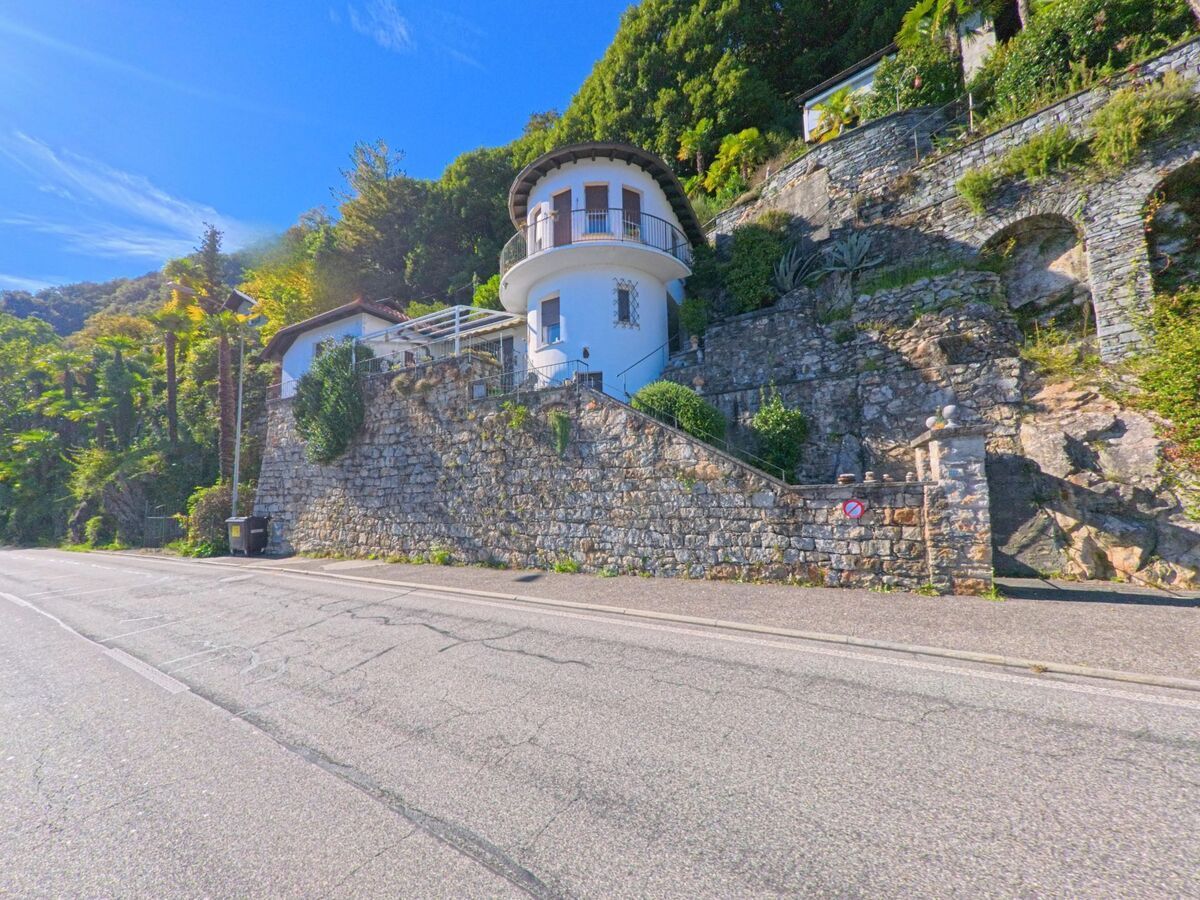 Ein rundes Haus mit Steinmauer erhebt sich an einer Hangstrasse in Ronco sopra Ascona (6613, Kanton Tessin) umgeben von dichter Vegetation.