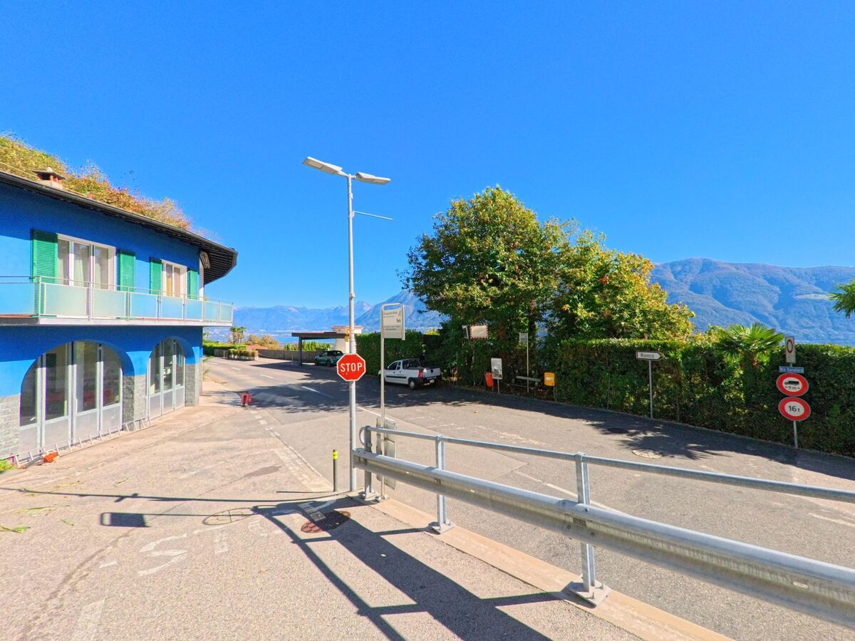 In Ronco sopra Ascona (6622, Kanton Tessin) steht ein blaues Haus an einer Kreuzung mit Stoppschild und Aussicht auf die umliegenden Berge.