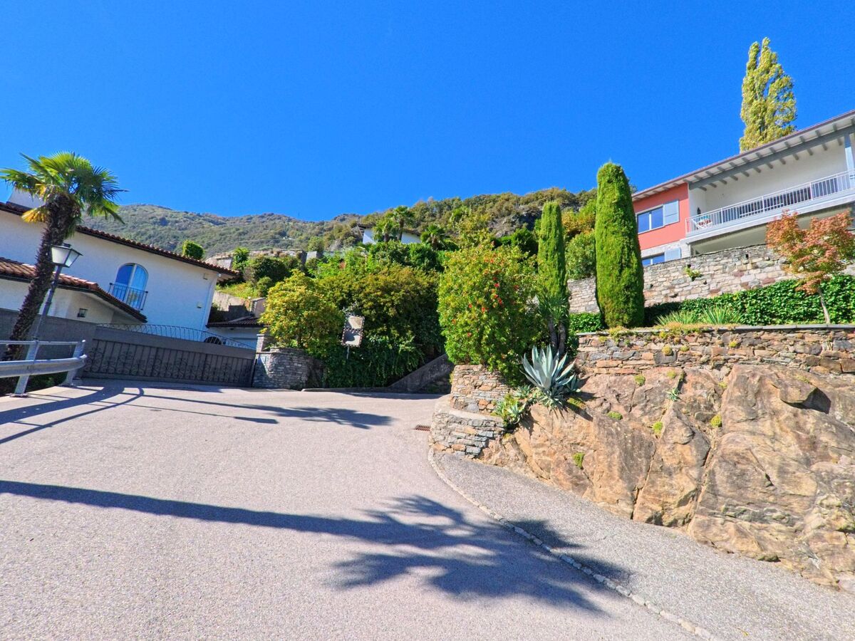 Eine steile Strasse mit gepflegten Häusern und Felsen führt in Ronco sopra Ascona (6622, Kanton Tessin) bergauf durch ein ruhiges Wohngebiet.