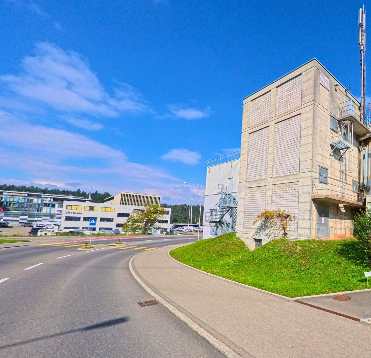 An einer geschwungenen Strasse erhebt sich ein Industriegebäude im Gewerbegebiet von Root (6037, Kanton Luzern).