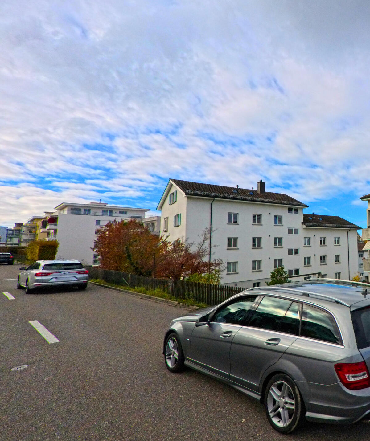 Eine Wohnstrasse mit Mehrfamilienhaeusern und parkierenden Autos fuehrt durch Rorschacherberg (9404, Kanton St. Gallen).