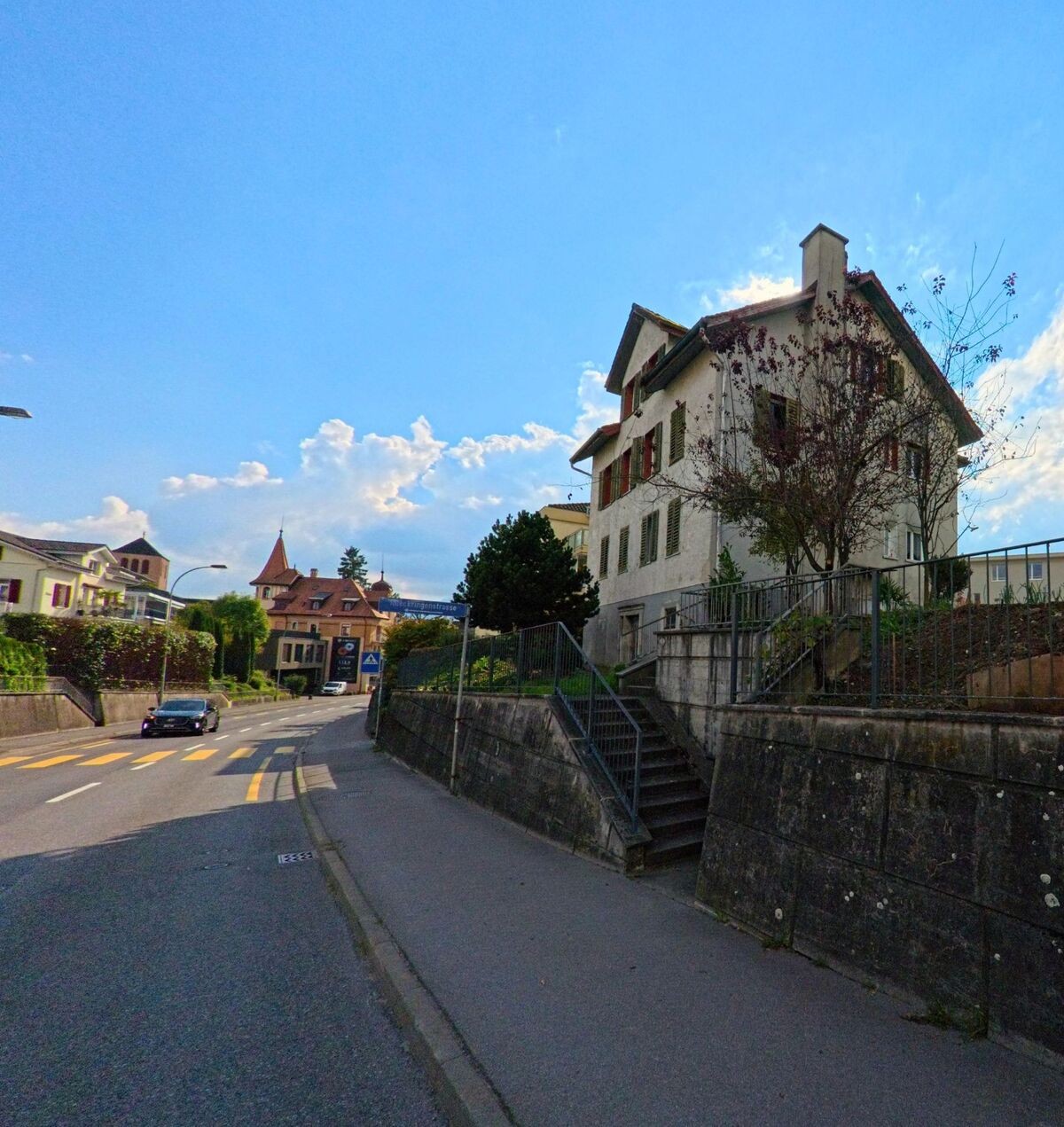 Eine steil ansteigende Strasse führt an einem älteren Wohnhaus in Rothenburg (6023, Kanton Luzern) vorbei.
