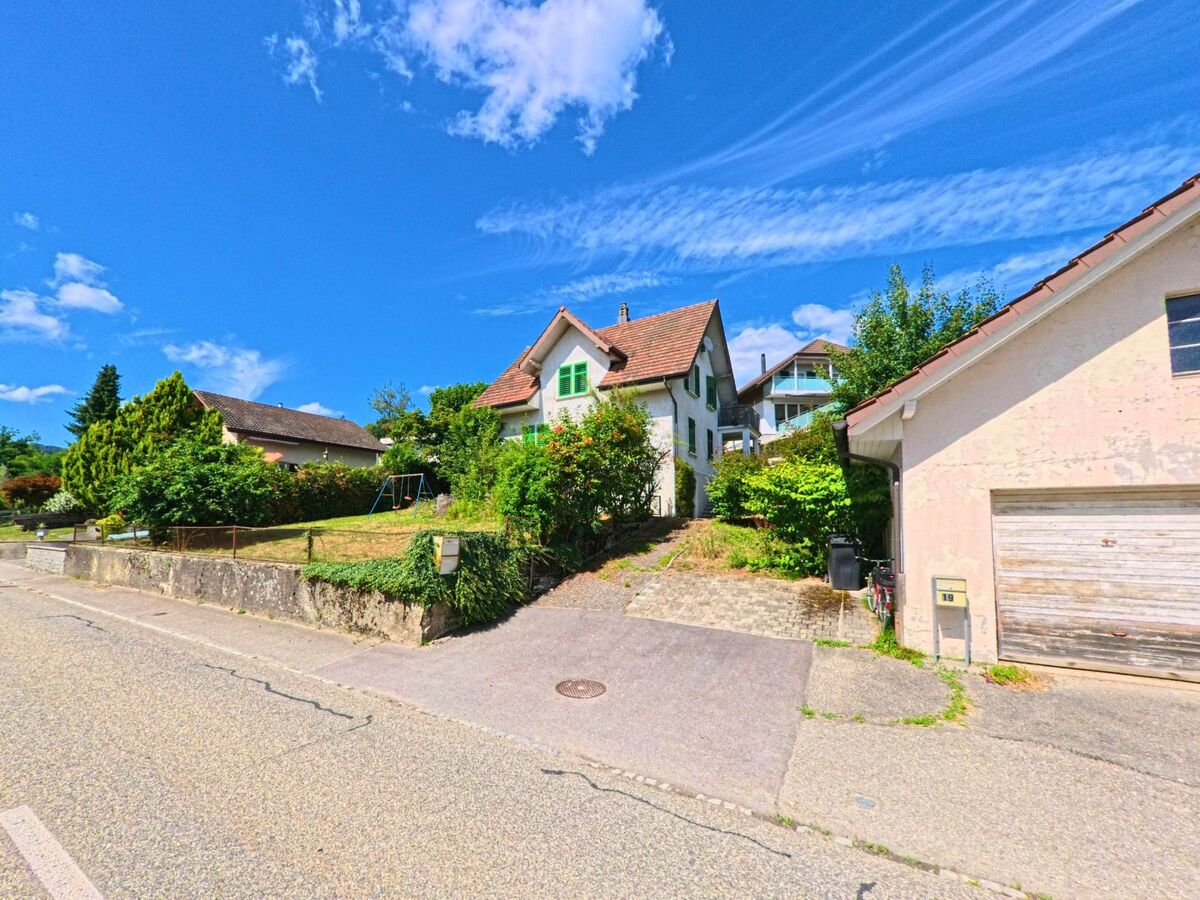 Ein kleines Wohnhaus mit gruene Fensterlaeden liegt in Rothrist (4852, Kanton Aargau) oberhalb der Strasse auf einem leicht ansteigenden Grundstueck mit Spielgeruest im Vorgarten.