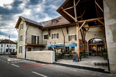 Die Rôtisserie de la Ferme in Collex-Bossy (1239, Kanton Genf) befindet sich in einem renovierten Bauernhaus mit Holzbalken und einer gemütlichen Terrasse mit blauen Sonnenschirmen.
