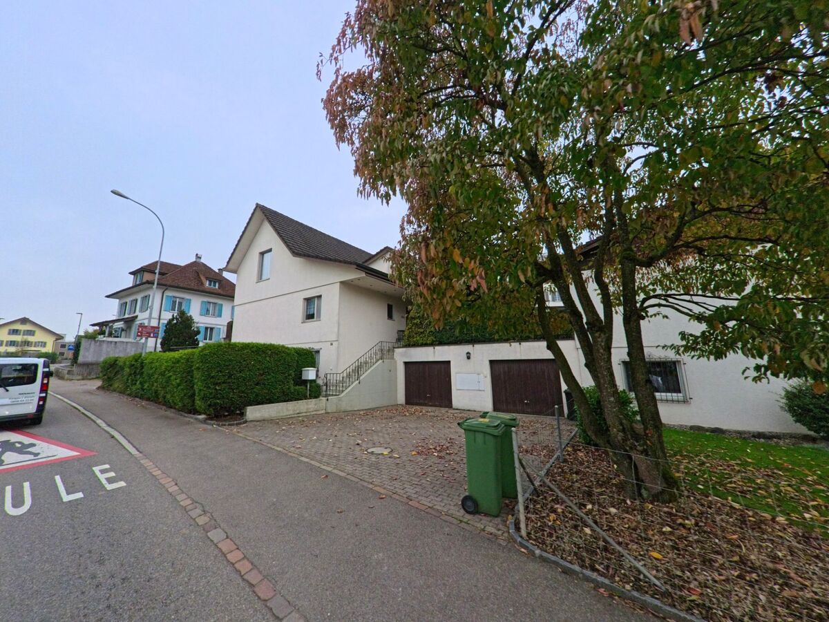 Ein Einfamilienhaus mit Garagen und herbstlichem Baum steht in Rottenschwil (8919, Kanton Aargau) an einer Strasse mit Markierung fuer den Schulbereich.