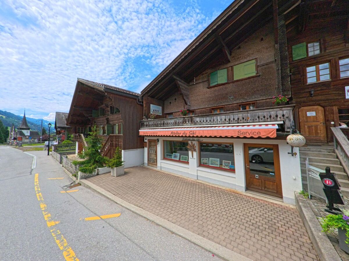 In Rougemont (1659, Kanton Waadt) befindet sich ein Sportgeschäft mit orangefarbener Markise in einem traditionellen Holzgebäude, nahe der Kirche und entlang der Dorfstrasse.