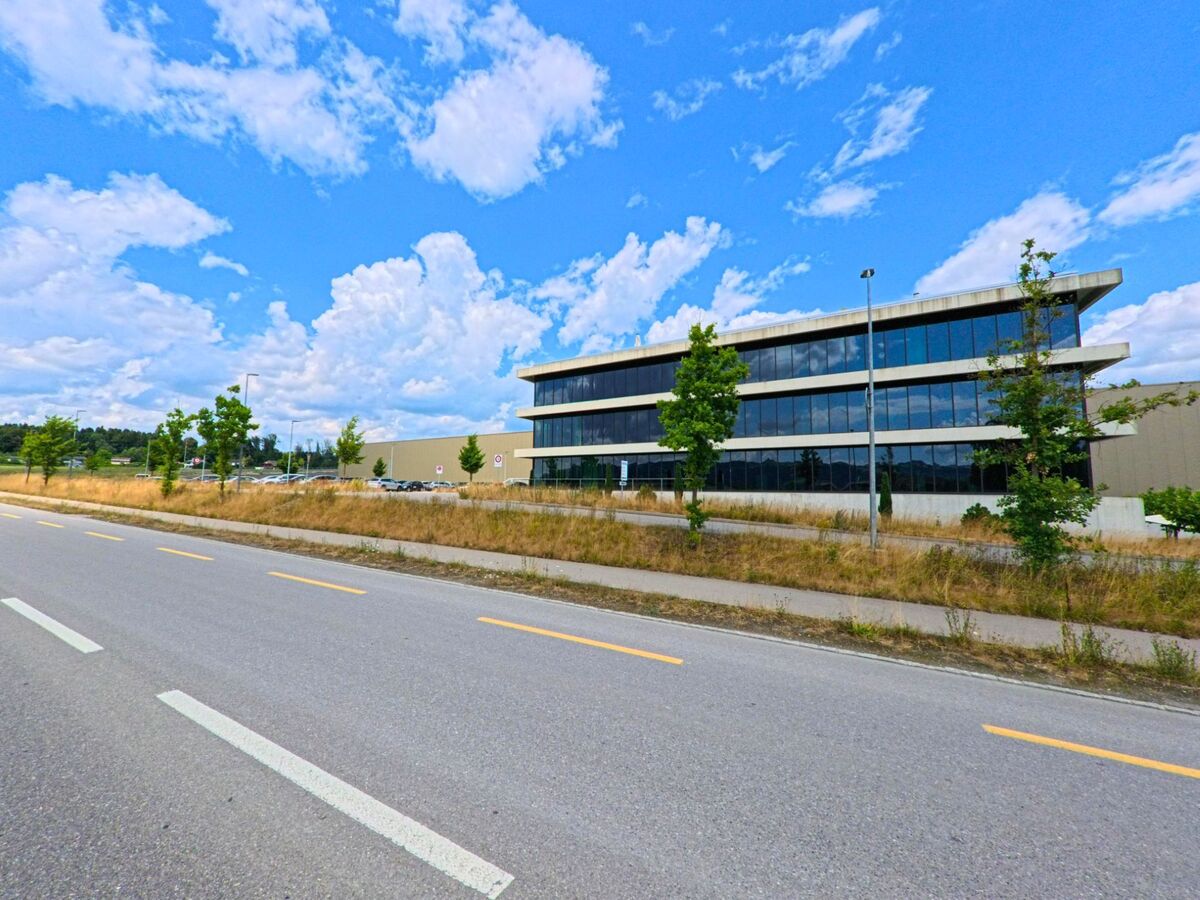 In Rubigen (3113, Kanton Bern) steht ein modernes Bürogebäude mit grossflächiger Glasfassade entlang einer verkehrsarmen Ausfallstrasse im Gewerbegebiet.
