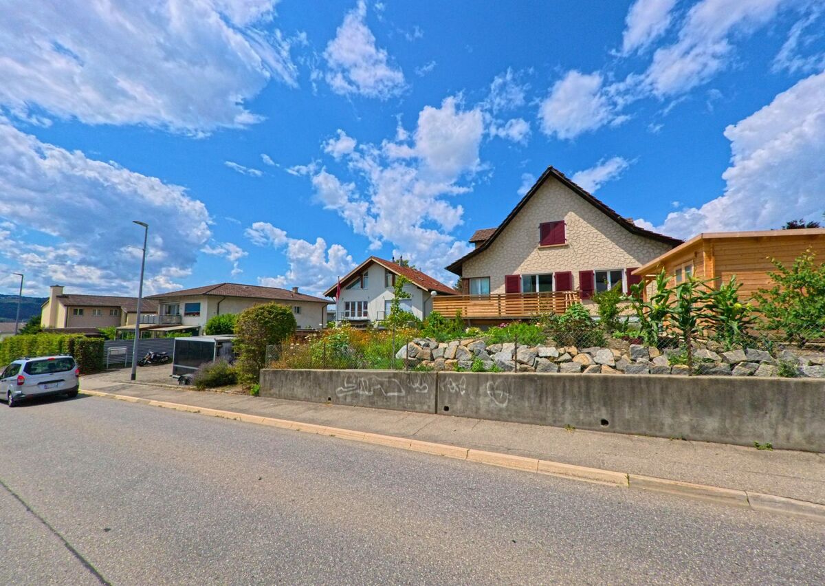 In einem ruhigen Wohnquartier von Rubigen (3113, Kanton Bern) stehen Einfamilienhäuser mit gepflegten Vorgärten und einer Natursteinmauer entlang der Strasse.