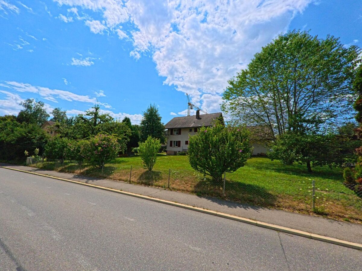 In Rubigen (3113, Kanton Bern) steht ein Einfamilienhaus mit grosszügigem Garten und blühenden Sträuchern hinter einem Drahtzaun an einer ruhig gelegenen Strasse.