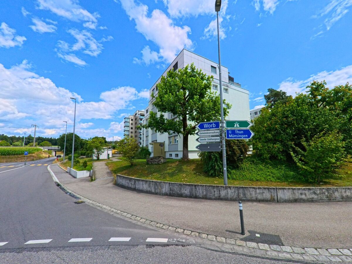 Wegweiser in Rubigen (3113, Kanton Bern) zeigen an einer Kreuzung die Richtung nach Worb, Thun und Münsingen, flankiert von Wohnhäusern und einem begrünten Strassenrand.