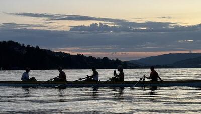 Mitglieder des Ruderclubs Rigi Küssnacht aus Küssnacht (6403, Kanton Schwyz) rudern bei Abendstimmung gemeinsam in einem langen Ruderboot über den See.