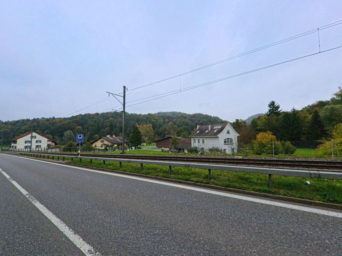Entlang der Bahnlinie in Rudolfstetten-Friedlisberg (8964, Kanton Aargau) stehen mehrere Einfamilienhäuser vor einem bewaldeten Hügel.