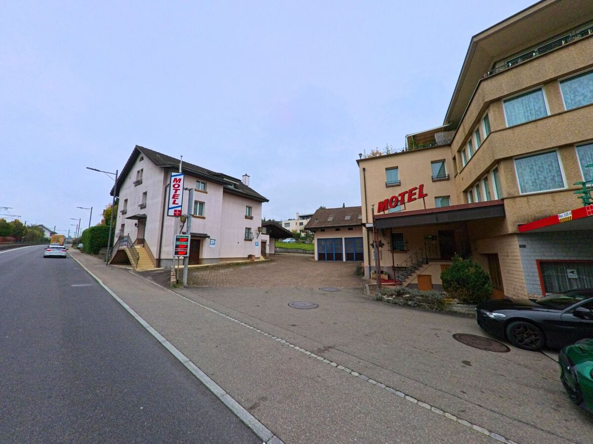 An der Hauptstrasse von Rudolfstetten-Friedlisberg (8964, Kanton Aargau) befindet sich ein Motel mit Parkplatz und angrenzenden Wohnhäusern.