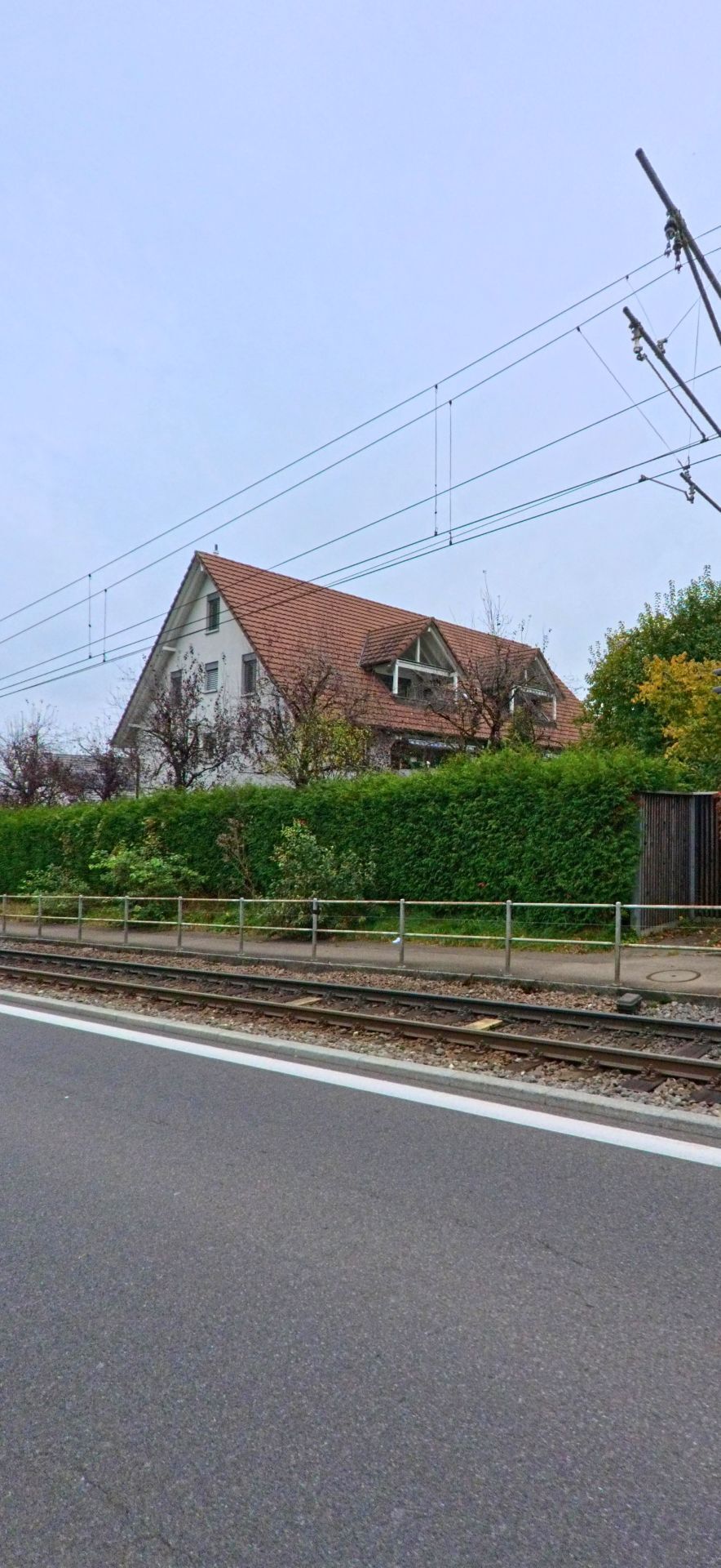 Ein Wohnhaus mit rotem Dach und dichter Hecke steht in Rudolfstetten-Friedlisberg (8964, Kanton Aargau) direkt neben den Bahngleisen.