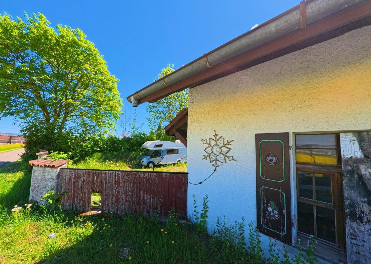 Am Rand eines Grundstücks in Rümlang (8153, Kanton Zürich) steht ein Wohnmobil im Grünen, während die weisse Hauswand im Vordergrund mit dekorativen Elementen geschmückt ist.