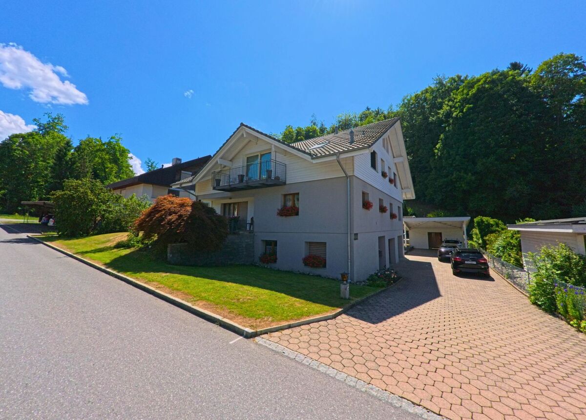 Ein modernes Wohnhaus mit gepflegtem Vorgarten und gepflasterter Einfahrt steht an einer ruhigen Seitenstrasse in Rüschegg (3154, Kanton Bern).