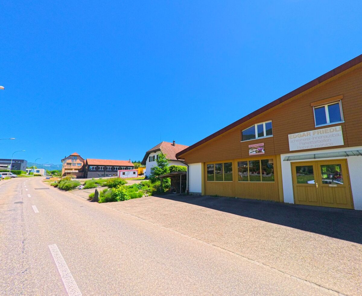 In Rüttenen (PLZ 4522, Kanton Solothurn) befinden sich entlang einer sonnigen Strasse Gewerbe- und Wohnhäuser mit Sicht auf das hügelige Umland.