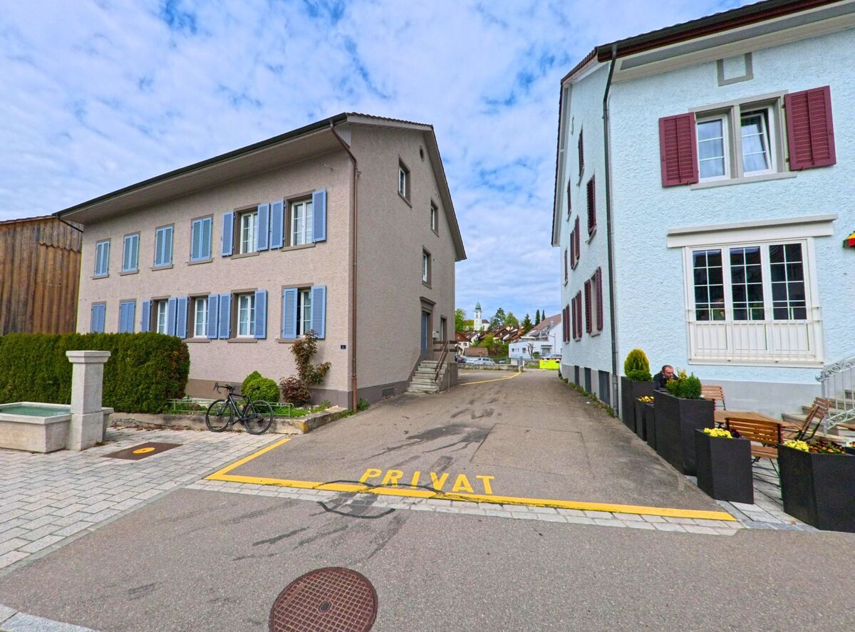 Zwischen zwei Wohnhäusern in Russikon (8332 im Kanton Zürich) verläuft eine private Zufahrt mit Blick auf den Kirchturm im Hintergrund.