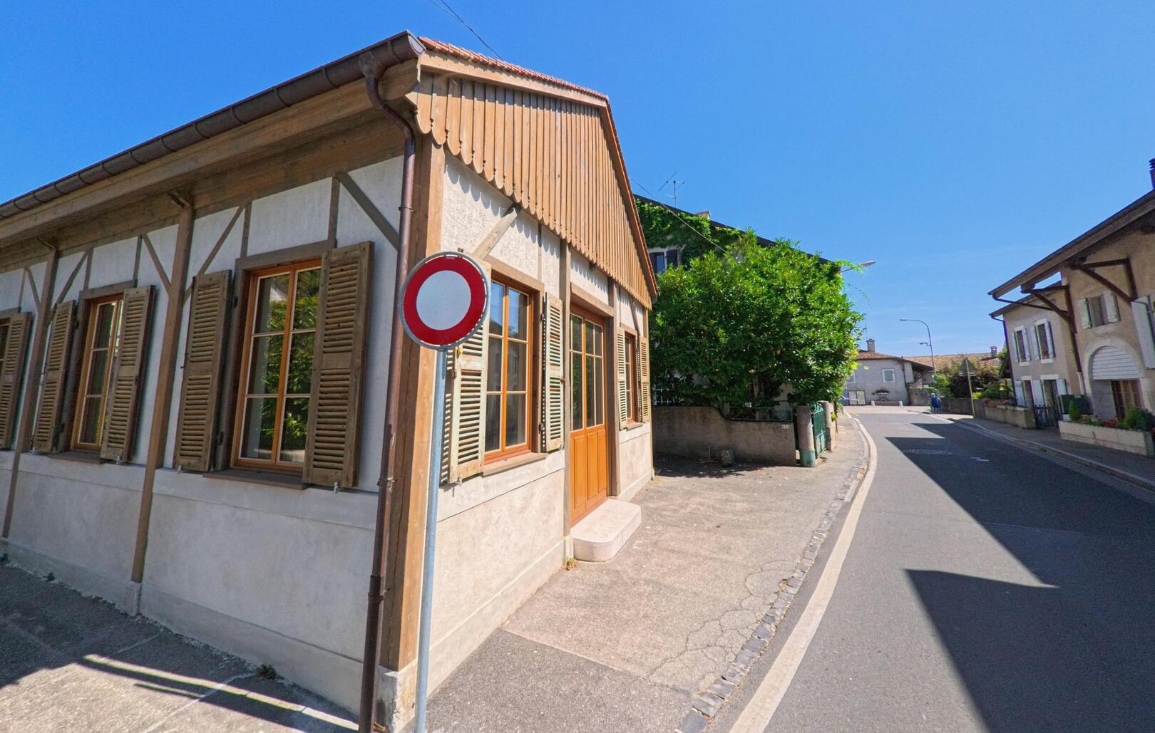 In Russin (1281, Kanton Genf) steht ein traditionelles Haus mit Holzfenstern und einem Tempo-30-Schild an einer schmalen Dorfstrasse.